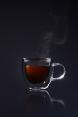 Steamy hot tea in a small glass against a black backdrop. Perfect for cozy café vibes or illustrating a calming moment
