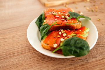 Fresh smoked salmon on toast with spinach and seeds. A healthy and delicious sandwiches on a wooden table.