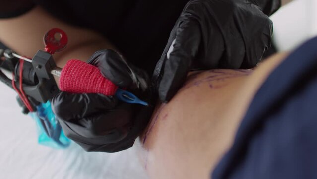 Close up shot of female tattooist in rubber gloves wiping skin of client and drawing tattoo contour with gun
