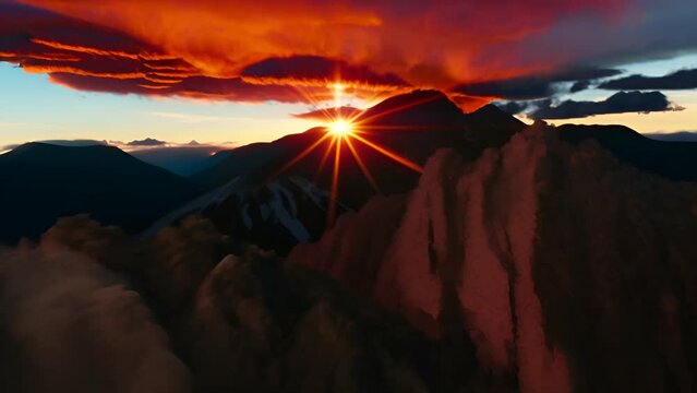 Golden Sunrise Over Majestic Mountains - The sun is visible at the horizon level and emits a bright starburst effect. The sky is painted with hues of orange and red 
