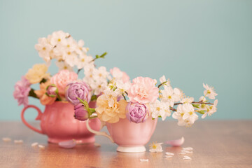 beautiful spring flowers in two cups in pastel colors on blue background