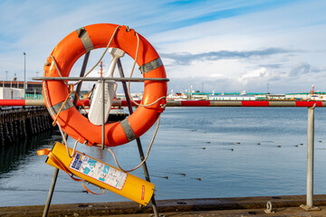 Orange lifebuoy on stand near fence of seaside