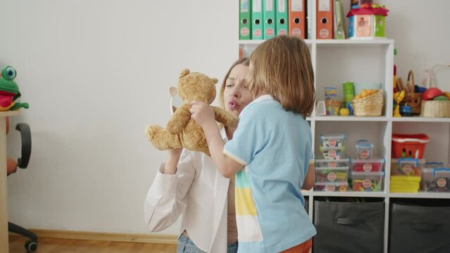 In the therapist's office, language blooms through games. Child, tutor in white, laugh and learn, a journey of words.