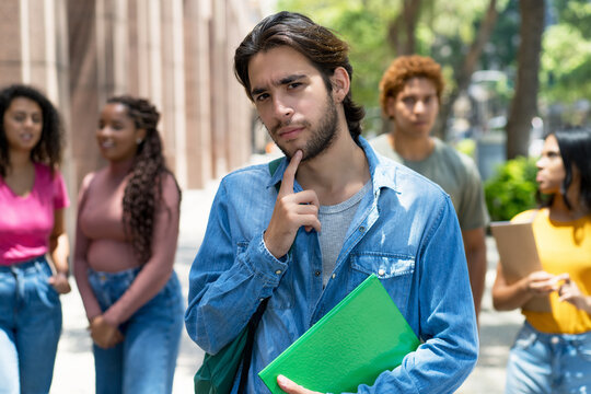 Smart latin american male student with group of caucasian and african american young adults