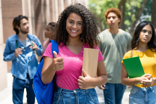 Latin american female student showing thumb up with group of caucasian and african american young adults