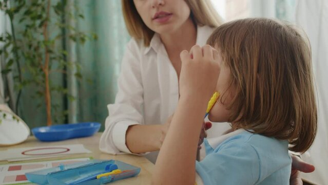 Language therapy: girl, tutor bond over letters, games. Office filled with happy learning, articulation joy.