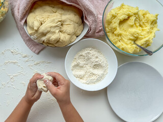 The hands of child knead the dough for making pies on white table, top view.
