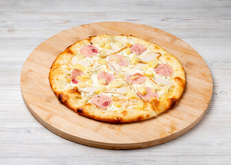 Italian Hawaiian pizza with ham and pineapples on a wooden board