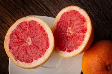 Red grapefruit sliced on a white plate, sitting on a dark wooden table.