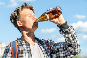 Joyful boy drinking lemonade from a glass bottle against a beautiful sky backdrop. He wears a plaid shirt and a backpack. Vibrant colors - 729952704