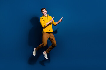 Fototapeta na wymiar Full length photo of nice young male jumping point empty space dressed stylish yellow garment isolated on dark blue color background