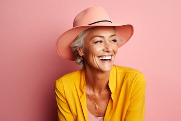 Portrait of smiling senior woman in hat and yellow shirt on pink background
