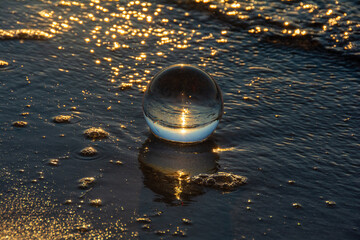 Glass ball lies in the water in the waves at the sea