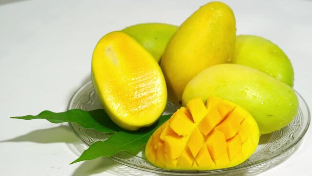 Close-up of the golden mangoes in a glass plate, mangoes and their sectional schematics; the furthest to the right is the common way of cutting when eating mangoes.