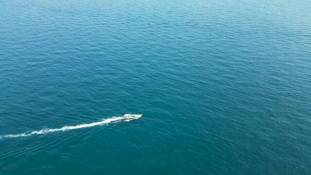 Long tail boat reaching Mango Bay Ko Tao Island Thailand shore with rocky peninsula, Aerial pan right shot