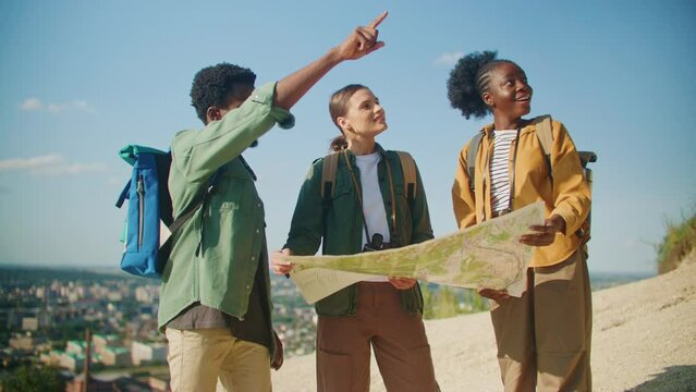 Camera view of group of multi-ethnic friends hiking together. Checking on physical map where to go next. Looking for trail or location for camp. Deciding together what to see next. Active lifestyle.