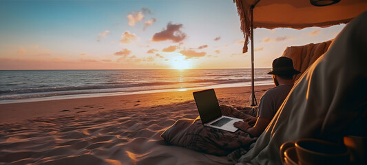 A digital nomad in the sands of a beach with a notebook working in the sunset, sitting close to the shoreline, sun, sky, horizon, ocean waves and seascape in the background. AI generated image. - obrazy, fototapety, plakaty