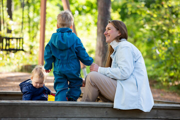 The mother with two children is having a fun time at the playground. Two little boys with their mom playing in the sandbox