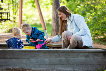 The mother with two children is having a fun time at the playground. Two little boys with their mom playing in the sandbox