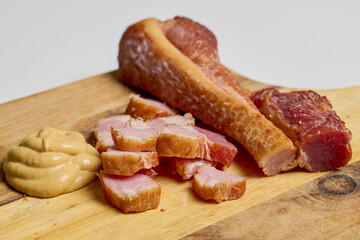 Ham cut into pieces and mustard on a wooden plate.