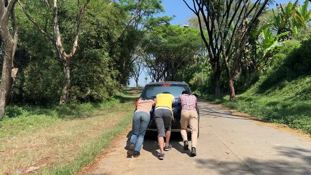 Rear View of Young Friends Pushing Car Along Countryside Road, Car Breakdown During Road Trip.