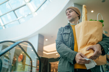 Man holds paper bag filled with various food items in his hand in mall