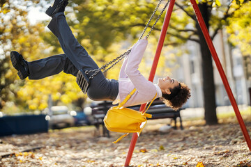 A playful young woman is swinging on the swing in city park.