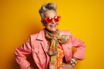 Portrait of a happy senior woman in pink jacket and sunglasses over yellow background