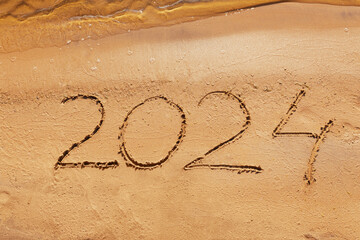 Hand-drawn numbers 2024 of new year on wet yellow sand on beach,