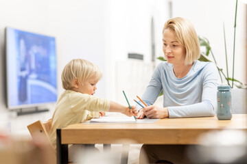 Caring young Caucasian mother and small son drawing painting in notebook at home together. Loving mom or nanny having fun learning and playing with her little 1,5 year old infant baby boy child