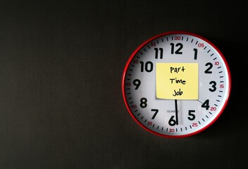 Red clock on dark black wallpaper with copy space , with yellow stick note written PART TIME JOB ,...