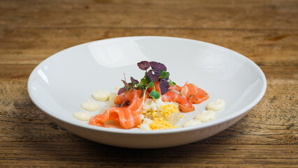 Smoked salmon appetizer with salad on white plate on wooden table in restaurant