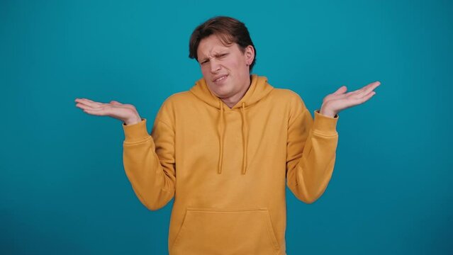 Dont know, who cares. Confused man shrugging shoulders, looking with uncertain clueless expression, demonstrating indifference doubts. Indoor studio blue background