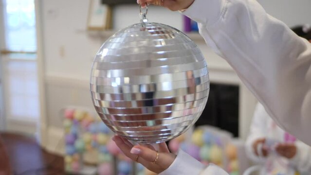 Spinning shiny silver disco ball in hand and preparing room for party.