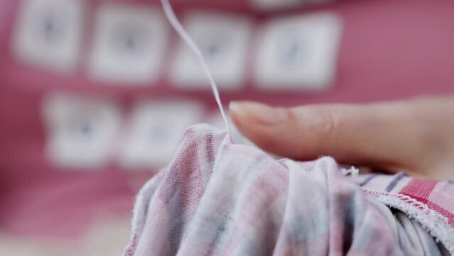 Hands of a woman sewing a pajama by hand, selective focus with blurred background.