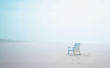 Fototapeta na wymiar Lonely chair on white sand of tranquil beach of sea covered with mist. Generative AI