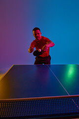 Intense table tennis rally. Portrait of young man player in motion in red neon light against white background. Dynamic gel portrait. Concept of professional sport, healthy lifestyle and recreation. Ad