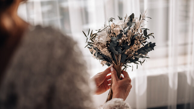 wedding bouquet in boho style collected from wild flowers, the bride holds a bouquet in her hand, in nature, white dress, live plants, a composition of dried flowers