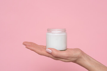 Female hands with cream on pink background.