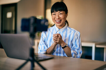 A smiling woman filming a video over the laptop, making a vlog while working over the laptop.