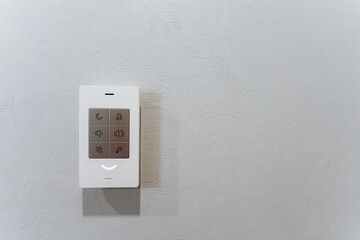An electronic device, resembling a rectangular gadget, hanging on the wall with a white remote control.