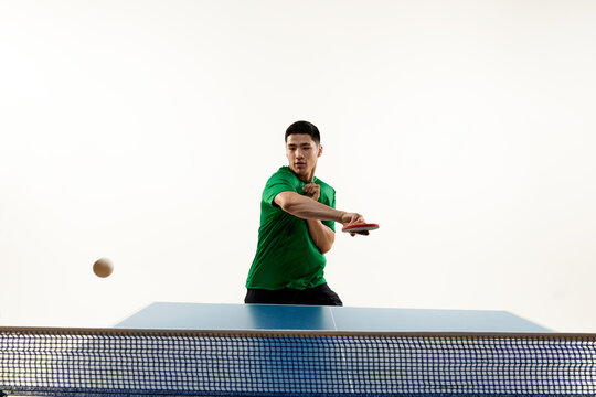 Athletic table tennis stance from competitive Asian sportsman, player in sportswear in motion against white studio background. Concept of sport, hobby, lifestyle, match, victory, championship.