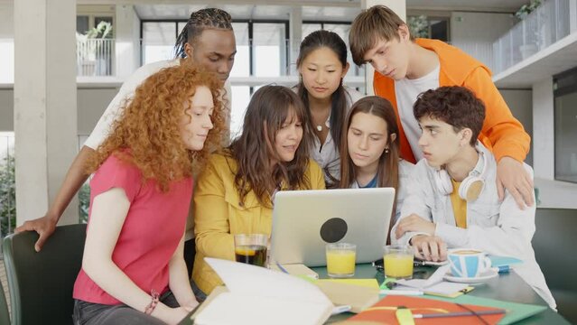 Multiracial university students sitting together at table with books and laptop - Happy young people doing group study in high school library - Life style concept with guys and girls in college campus
