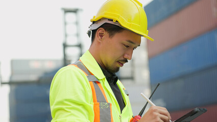 Young asian Japanese foreman in hardhat and safety uniform working on tablet checking inventory...