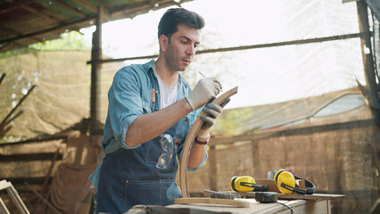 Young carpenter man using pencil to mark on timber during work with in wood factory workplace....