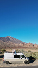 Two individuals sitting atop a van parked on the Teide Volcano Mountain in Tenerife, enjoying the scenic view.