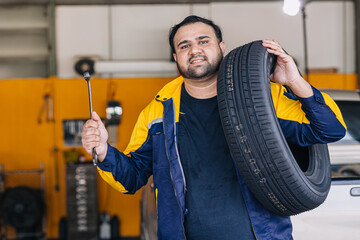 Portrait Indian man worker in garage auto mechanic happy work car service replace tyre vehicle maintenance - obrazy, fototapety, plakaty