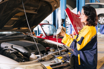 Garage auto mechanic women worker working check engine oil level stick in car service center...