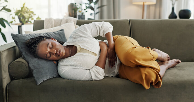 Home, pain and black woman on a couch, cramps and stomach with sickness, suffering and disease in the living room. African person, apartment and girl with abdominal problem, tummy ache and period
