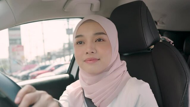Beautiful white Muslim woman covers her hair with a hijab and wears a seat belt while driving a car.